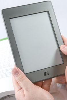 Man hands holding  an electronic book reader with blank screen, open books in the background