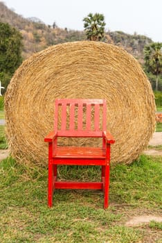 Large rounded hay stack on green grass with red chair in front, taken outdoor