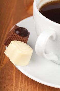 Cup of coffee with chocolate candies on a wooden table