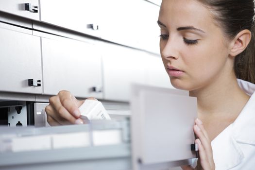 Young woman pharmacist taking medicine from drawer