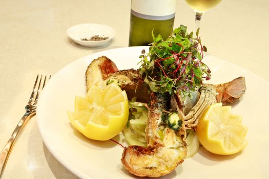 Gourmet grilled lobster or crayfish served with decoratively cut lemon and a topping of fresh herb salad