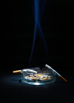 Dirty Ashtray And Two Cigarette On the Dark Background