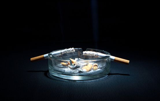 Dirty Ashtray And Two Cigarette On the Dark Background