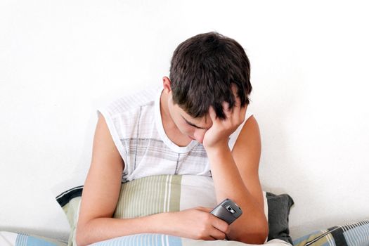 Sad Teenager sitting with pillow and mobile phone on the Bed in Home interior