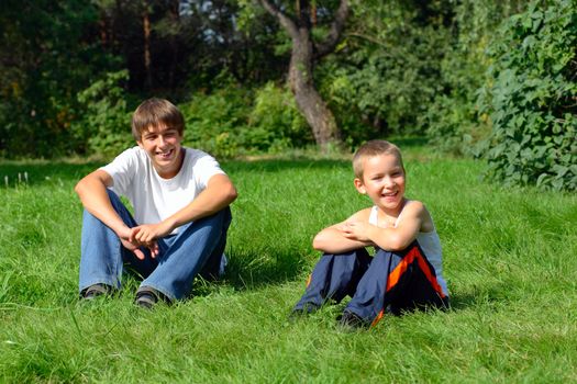 Happy Brothers sit on the grass in the summer park