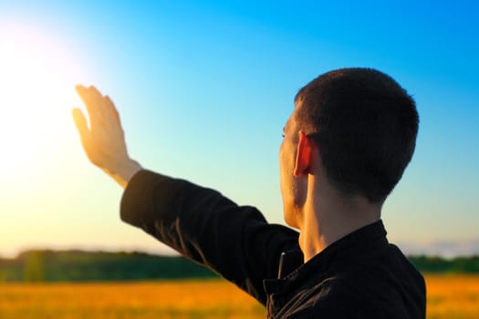 Young Man stretch his Hand to the Sunlight in the Evening Fields