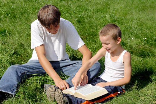 Older and Little Brothers reads a Book in the Summer Park