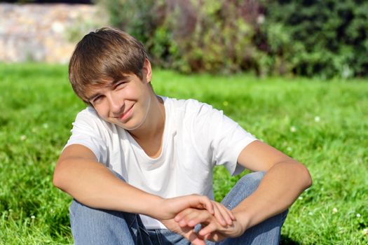 Happy Teenager sit on the Grass in the Summer Park