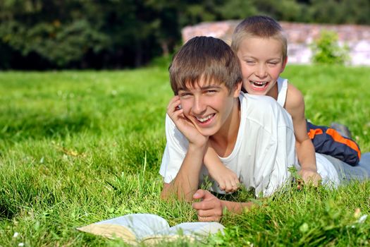 Happy Brothers lying on the Grass with a Book in the Summer Park