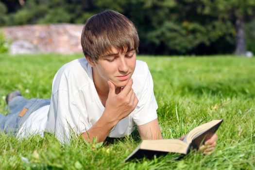 Happy Teenager lying on the Grass and reads a Book in the Summer Park