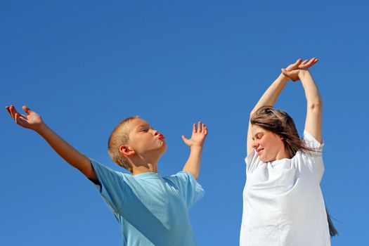 Young Boy and Teenage Girl with hands up on the Blue Sky Background