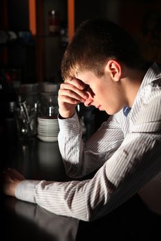 Sad and Lonely Young Man Sitting in the Darkness at the Bar counter