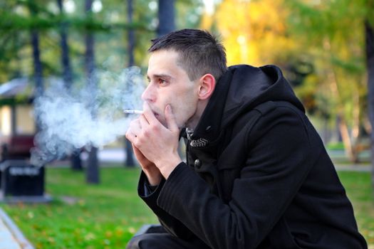 Sad man smoking cigarette in the autumn park