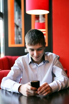 Cheerful Young Man Reading SMS on Mobile Phone at the Home