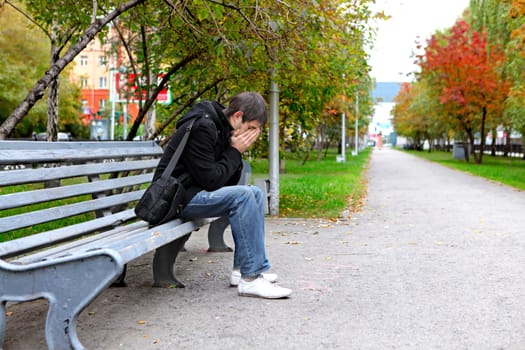 Sad young man sitting on the bench outdoor