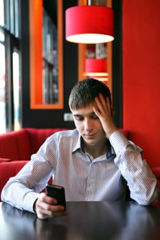 Sad Young Man with Mobile Phone at the table