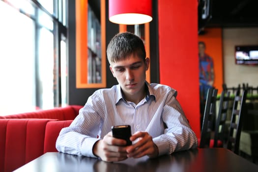 Sad Young Man with Mobile Phone at the table