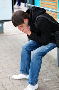 Sad Young Man Sitting at the Bus Stop at the City Street