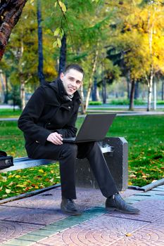 Happy Young man with Laptop sitting on the bench at the Autumn Park