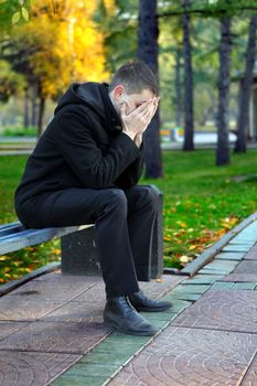 Sad young man sitting on the bench outdoor