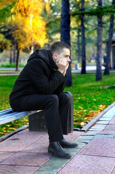 Sad young man sitting on the bench in the autumn park