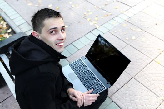Happy Young man with Laptop sitting on the bench at the Autumn Park