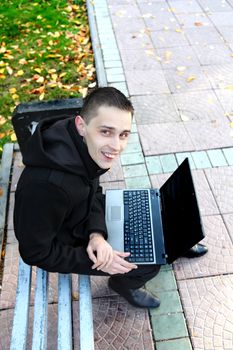 Happy Young man with Laptop sitting on the bench at the Autumn Park