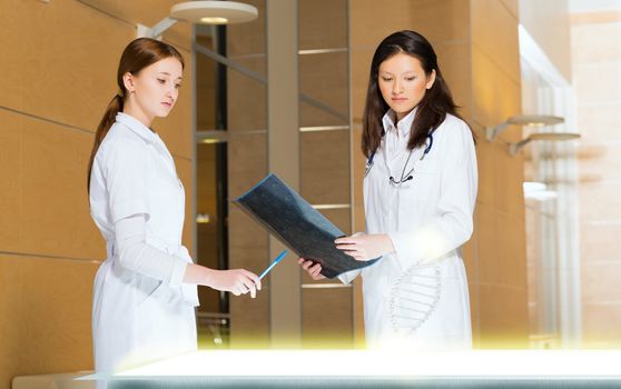 two doctors stand near glowing table discussing. projected objects on a desk