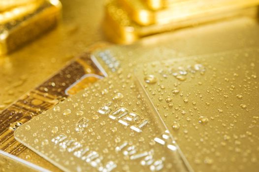 fine gold ingots and credit cards on a wet golden background