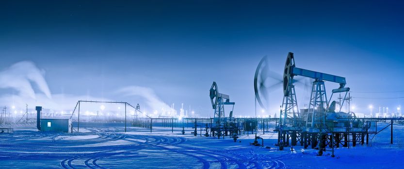 Oil and gas industry. Panoramic of a pumpjack and oil refinery in the winter with snow. Night view.