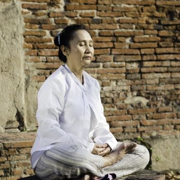 Buddhist woman meditating against ancient temple