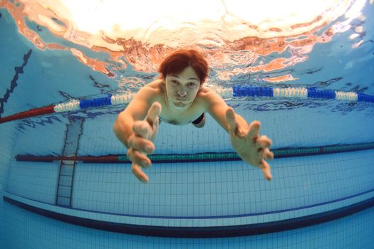 man underwater in swimming pool streching hands