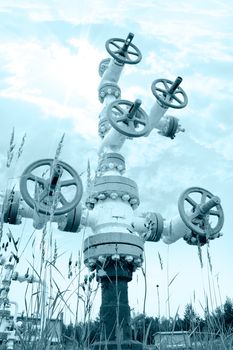 Oil industry. Wellhead with valve armature on a sky background. Toned.