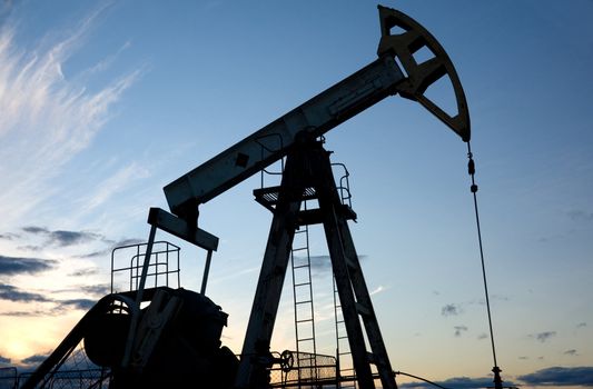 Silhouette pump jack on a blue sunset sky background.