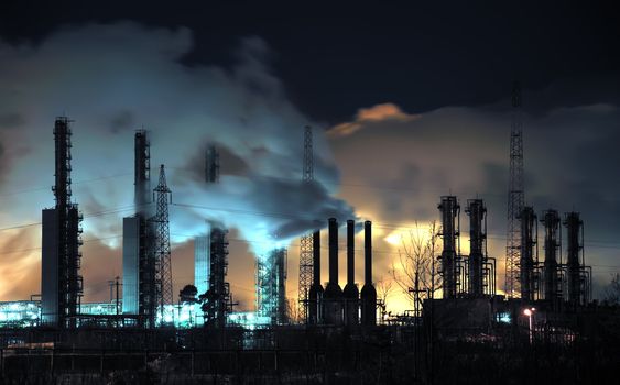 A brightly lit industrial site at night with plumes of smoke coming from chimneys. 
Russia, Western Siberia.