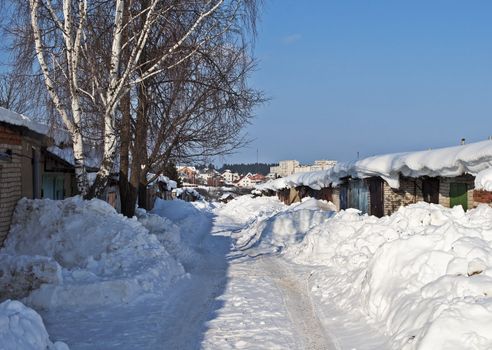 Road in snow among the snowdrifts along garages