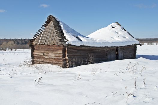 Old wooden barn with a snow-covered sagging roof, winter sunny day