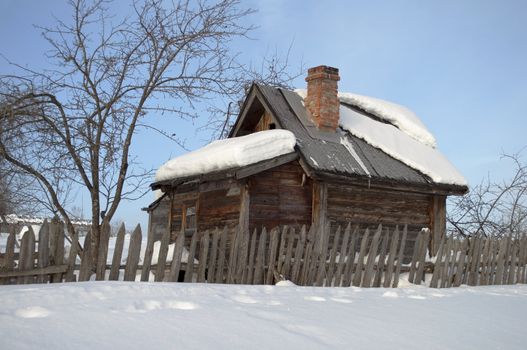 Old small wooden bathhouse among the snow drifts, winter sunny day