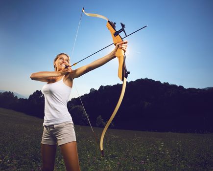 Attractive female archer bending a bow and aiming in the sky