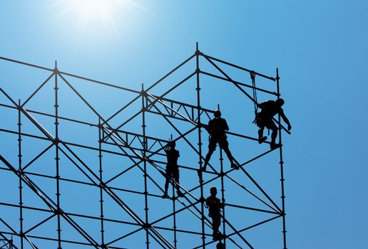 Silhouette of construction workers on scaffold working under a blue sky