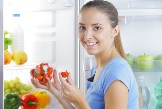Smiling girl with strawberries near the refrigerator