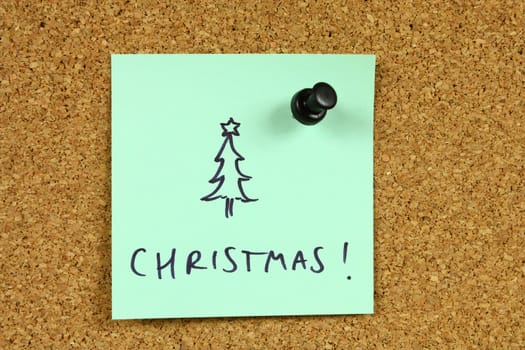 Green small sticky note on an office cork bulletin board. Celebrating Christmas. Christmas tree symbol.