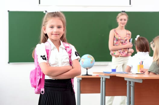 portrait of schoolgirl with a school backpack, in the background a classroom and the teacher tells the class