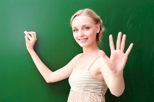 young beautiful teacher writes on the blackboard with chalk and shows five points