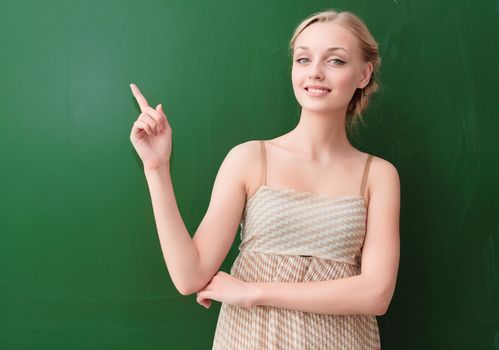 beautiful young teacher is standing near blackboard and points up
