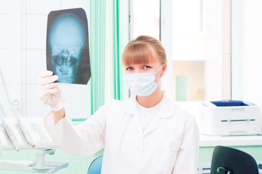 Young woman in protective mask dotstor looks at an X-ray of skull