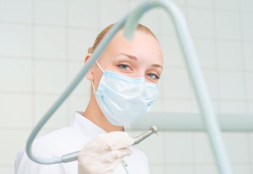 female dentists in protective mask holds a dental drill, the doctors at work