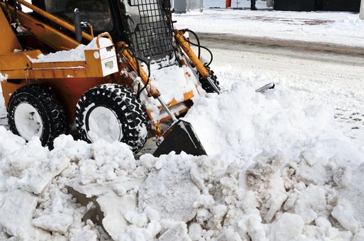 yellow tractor cleaning the snow on a street