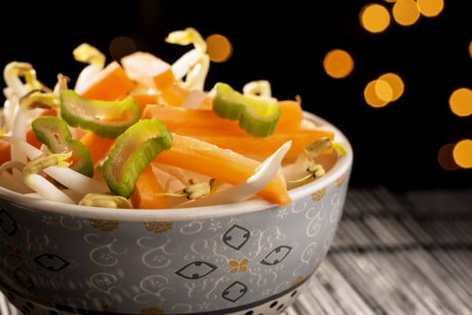 Closeup of a bowl with Asian vegetables on black bamboo mat and lights in the background