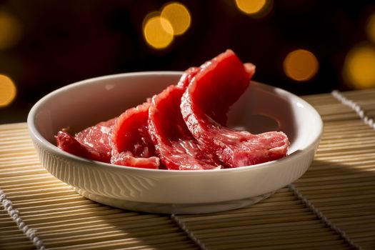 Sliced​​, red, raw meat in a white bowl on a bamboo mat